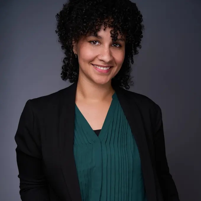 Professionelles Business-Portrait einer Frau vor neutralem Studiohintergrund; sie trägt eine schwarze Jacke und eine dunkelgrüne Bluse, steht aufrecht, lächelt freundlich und wirkt offen sowie kompetent – ideal für Unternehmenswebseiten, Teamvorstellungen und berufliche Profile.